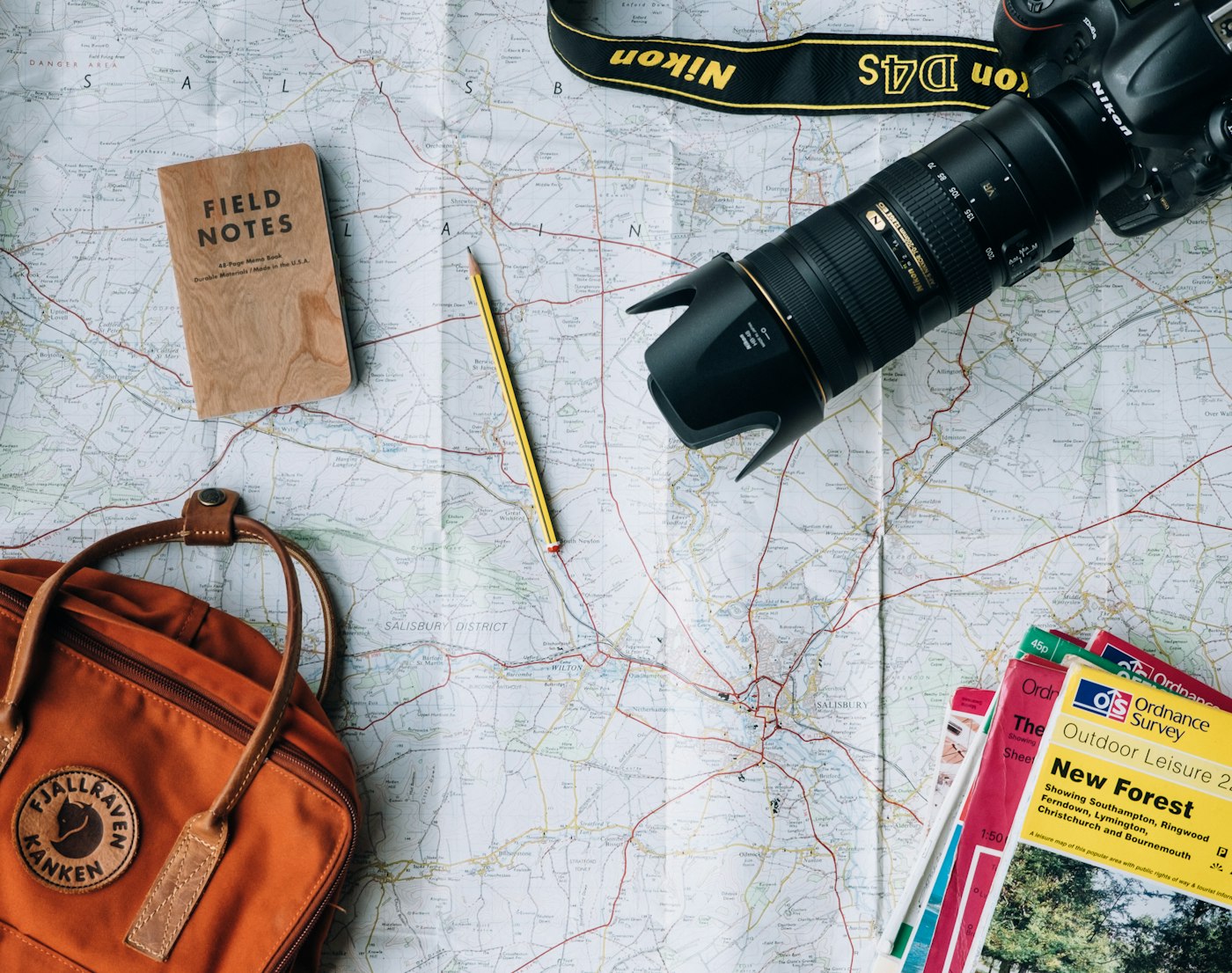 A map, camera, notebook and backpack laid out while planning a trip